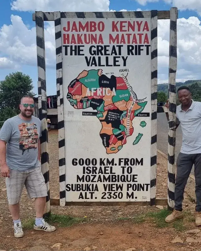 Two travellers standing beside the "Jambo Kenya" sign at the Subukia viewpoint over the Great Rift Valley, Kenya